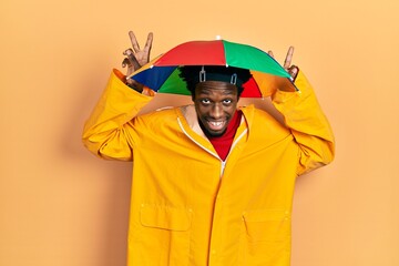 Young african american man wearing yellow raincoat posing funny and crazy with fingers on head as bunny ears, smiling cheerful