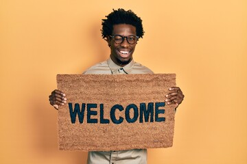 Young african american man holding welcome doormat winking looking at the camera with sexy...