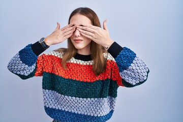Young hispanic girl standing over blue background covering eyes with hands smiling cheerful and...