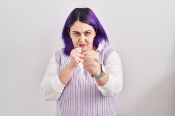 Plus size woman wit purple hair standing over white background ready to fight with fist defense gesture, angry and upset face, afraid of problem