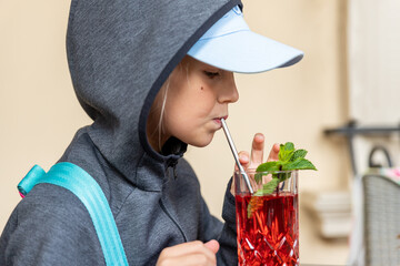 Profile portrait view of cute preteen little kid girl in grey hoodie enjoy drinkong healthy berry lemonade juice compote cocktail walking outdoors. Thirsty child drink beverage outside © Kirill Gorlov