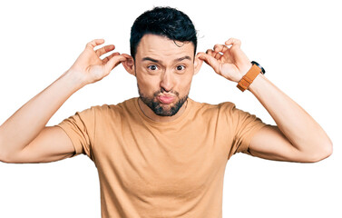 Hispanic man with beard wearing casual t shirt smiling pulling ears with fingers, funny gesture....