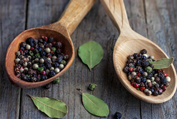 Spice peppers in wooden spoons with bay leaf on the table