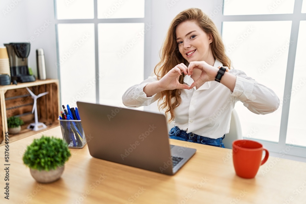 Poster Young caucasian woman working at the office using computer laptop smiling in love doing heart symbol shape with hands. romantic concept.