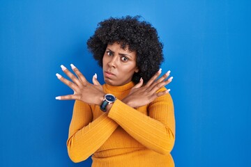 Fototapeta na wymiar Black woman with curly hair standing over blue background rejection expression crossing arms doing negative sign, angry face