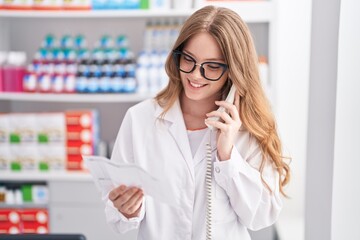 Young woman pharmacist talking on telephone reading prescription at pharmacy