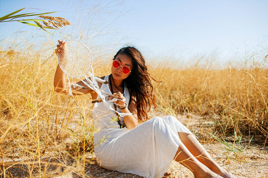 Asian Boho Chic In Long White Dress Holding Dream Catcher In Field With Dry Grass.