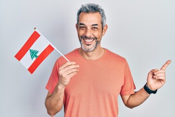 Handsome middle age man with grey hair holding lebanon flag smiling happy pointing with hand and...