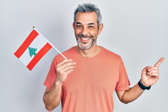 Handsome middle age man with grey hair holding lebanon flag smiling happy pointing with hand and finger to the side