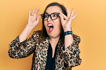 Middle age hispanic woman wearing business clothes and holding glasses angry and mad screaming...