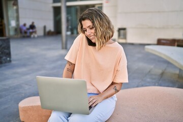 Young hispanic woman talking on the smartphone using laptop at street