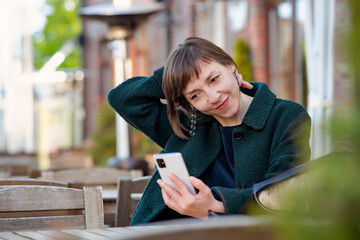 Woman sits in a cafe and looks at the phone and smiles - 517666344