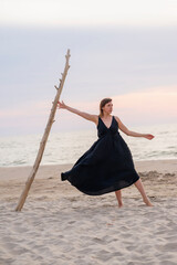 Woman in dress dances on the seashore near a tree