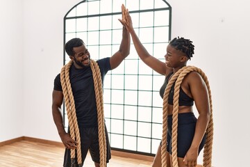 Young african american sporty couple smiling happy holding battle rope and high five at sport center. - Powered by Adobe