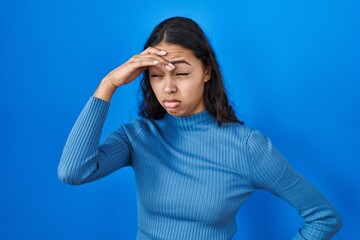 Young brazilian woman standing over blue isolated background worried and stressed about a problem with hand on forehead, nervous and anxious for crisis