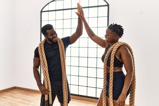 Young african american sporty couple smiling happy holding battle rope and high five at sport center.