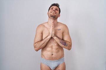 Fototapeta premium Young hispanic man standing shirtless wearing underware begging and praying with hands together with hope expression on face very emotional and worried. begging.
