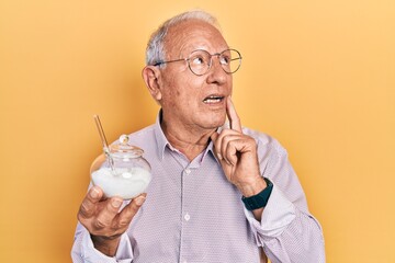 Senior man with grey hair holding bowl with sugar serious face thinking about question with hand on...