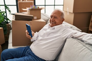 Senior man smiling confident using smartphone at new home