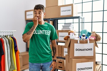 Young handsome hispanic man wearing volunteer t shirt at donations stand looking stressed and...