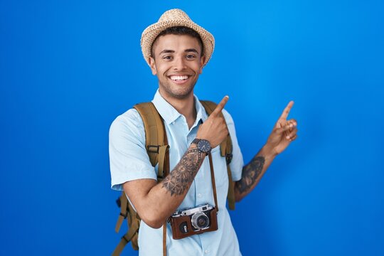 Brazilian Young Man Holding Vintage Camera Smiling And Looking At The Camera Pointing With Two Hands And Fingers To The Side.