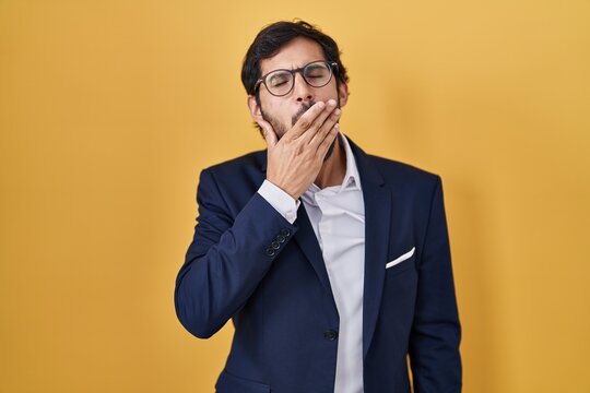 Handsome latin man standing over yellow background bored yawning tired covering mouth with hand. restless and sleepiness.
