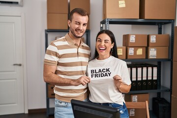 Young couple working at small business holding black friday banner winking looking at the camera...