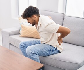 Young arab man suffering for backache sitting on sofa at home