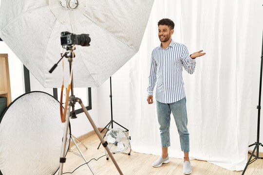 Arab young man posing as model at photography studio smiling cheerful presenting and pointing with palm of hand looking at the camera.