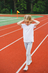 Obraz premium A little girl of 7-8 years old in a white t-shirt runs outdoors in the stadium. The girl is doing sports on a sunny day