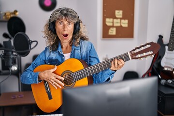 Fototapeta na wymiar Middle age woman playing classic guitar at music studio scared and amazed with open mouth for surprise, disbelief face