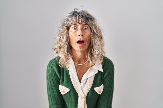 Middle age woman standing over white background afraid and shocked with surprise and amazed expression, fear and excited face.
