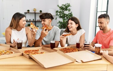 Fototapeta premium Group of young people smiling happy eating italian pizza sitting on the table at home