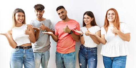 Fototapeta premium Group of young friends standing together over isolated background showing palm hand and doing ok gesture with thumbs up, smiling happy and cheerful