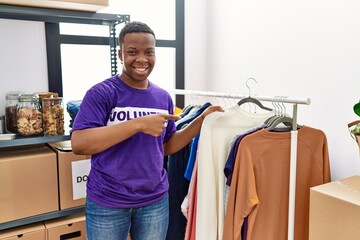 Young african man wearing volunteer t shirt at donations stand smiling happy pointing with hand and finger