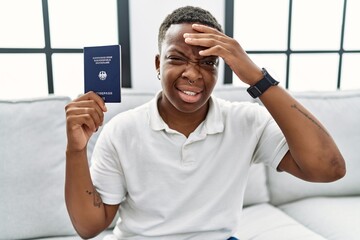 Young african man holding deutschland passport stressed and frustrated with hand on head, surprised and angry face