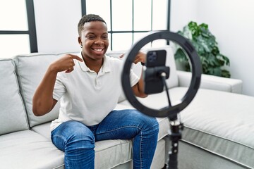 Young african man recording vlog tutorial with smartphone at home looking confident with smile on...