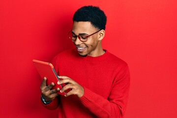 Young african american man using touchpad device looking positive and happy standing and smiling with a confident smile showing teeth