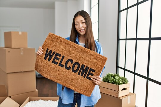 Young chinese girl smiling happy holding welcome doormat at new home