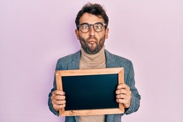 Handsome man with beard holding blackboard making fish face with mouth and squinting eyes, crazy and comical.