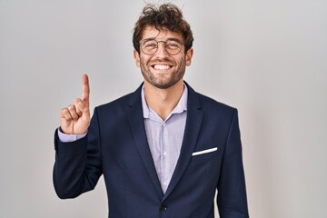 Hispanic business man wearing glasses showing and pointing up with finger number one while smiling confident and happy.