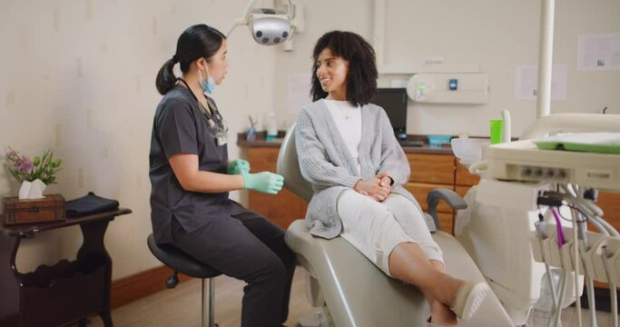 Female dentist consulting with a client on oral hygiene at a healthcare clinic. Orthodontist giving advice on teeth whitening procedure during a dental checkup with a patient while putting on gloves