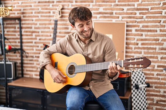 Young man musician smiling confident playing classical guitar at music studio