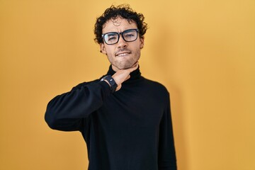 Fototapeta premium Hispanic man standing over yellow background cutting throat with hand as knife, threaten aggression with furious violence
