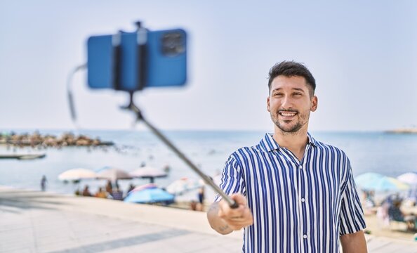 Young handsome man taking a photo using selfie stick by the sea
