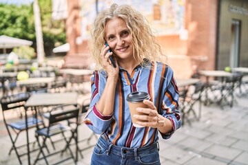 Middle age blonde woman talking on the smartphone drinking coffee at terrace coffee shop