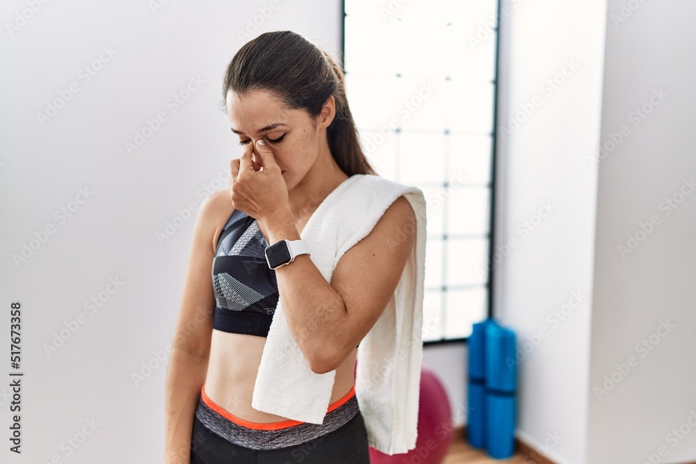 Poster Young brunette woman wearing sportswear and towel at the gym tired rubbing nose and eyes feeling fatigue and headache. stress and frustration concept.