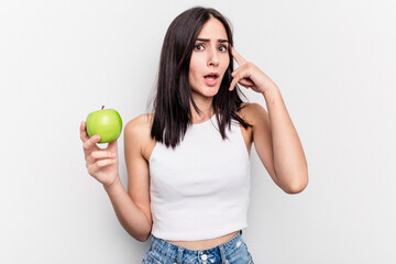 Young caucasian woman holding an apple isolated on white background showing a disappointment gesture with forefinger.
