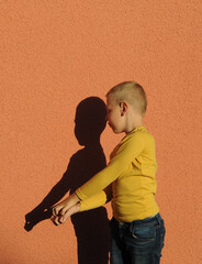 Boy playing in shadow theater, making crocodile on orange color background