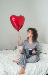 Young woman holding a heart balloon in bed